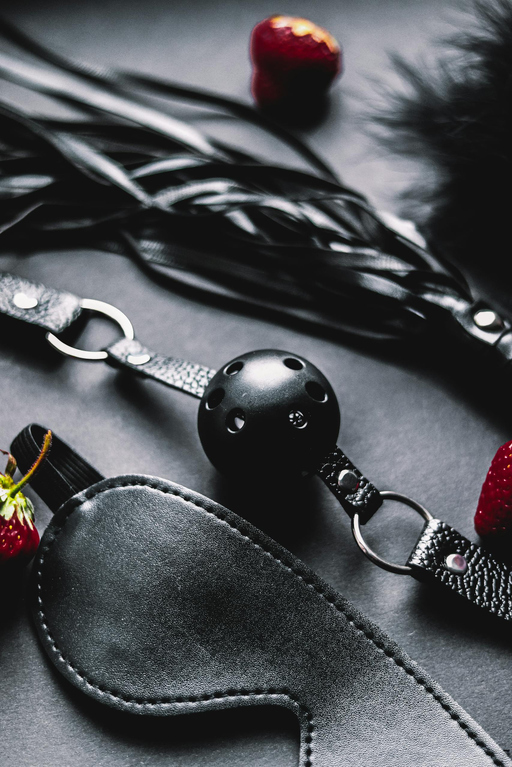 Close-up of BDSM gear including blindfolds and ball gags, with red strawberries.